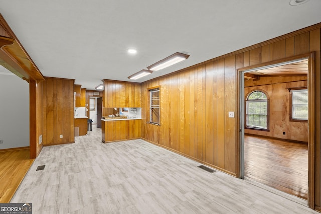 kitchen with kitchen peninsula, light hardwood / wood-style flooring, and wood walls