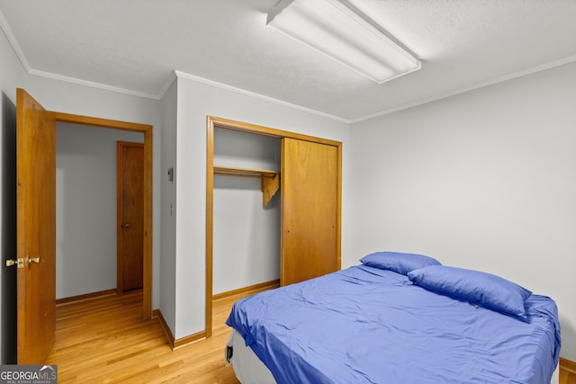 bedroom featuring a closet, light hardwood / wood-style floors, a textured ceiling, and ornamental molding