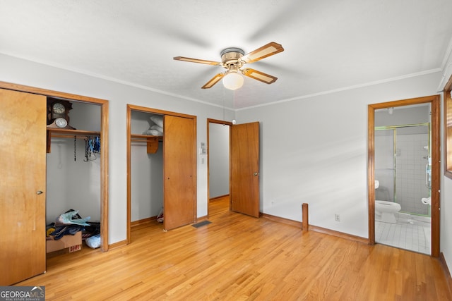 unfurnished bedroom featuring light wood-type flooring, ensuite bath, ceiling fan, crown molding, and multiple closets