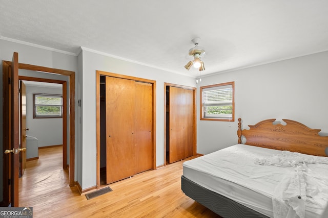 bedroom featuring ceiling fan, light hardwood / wood-style flooring, crown molding, and two closets