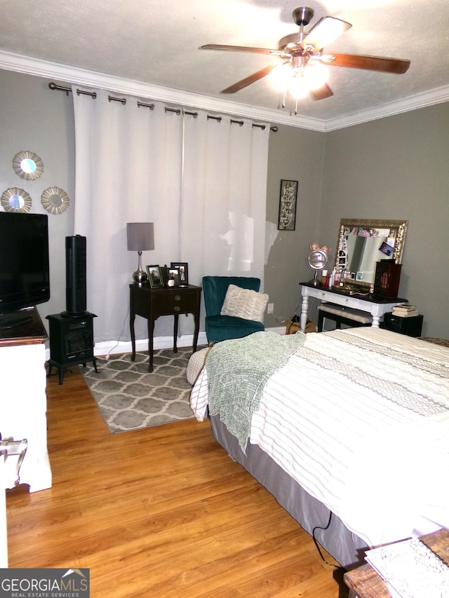 bedroom with ornamental molding, a textured ceiling, ceiling fan, hardwood / wood-style floors, and a wood stove