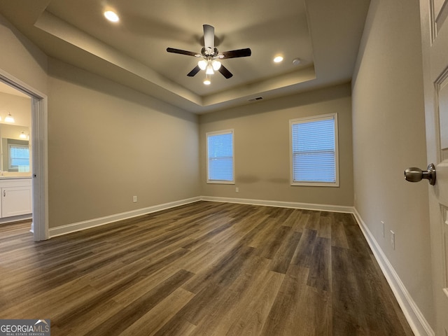 spare room with a tray ceiling, ceiling fan, and dark hardwood / wood-style flooring