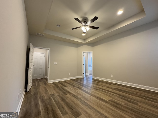 unfurnished room featuring ceiling fan, a raised ceiling, and dark wood-type flooring