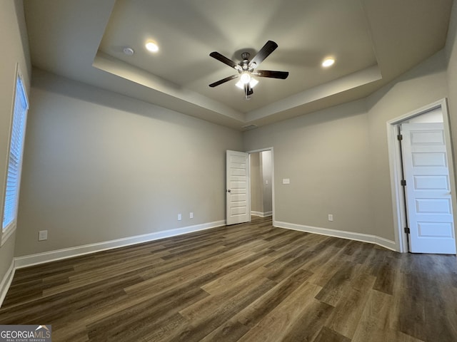 spare room with a tray ceiling, ceiling fan, and dark hardwood / wood-style floors