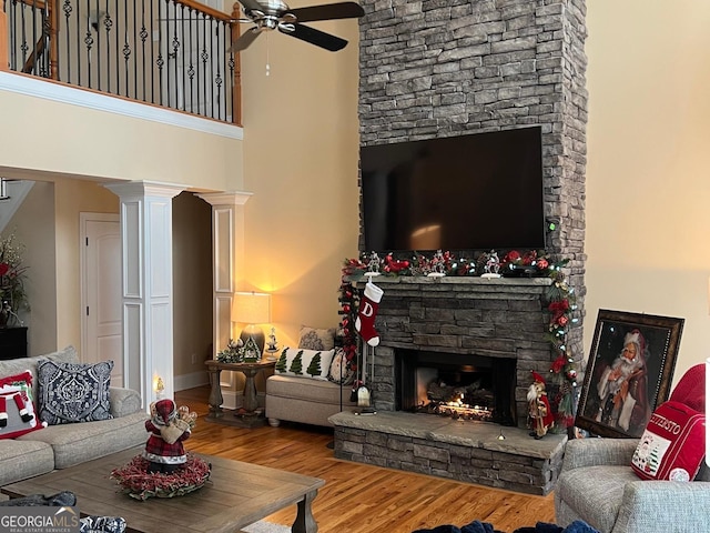 living room with a fireplace, wood-type flooring, ceiling fan, and a high ceiling