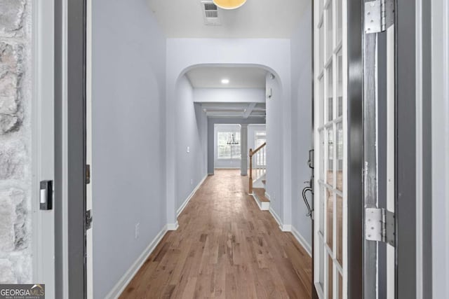 hallway featuring beamed ceiling, coffered ceiling, and light wood-type flooring