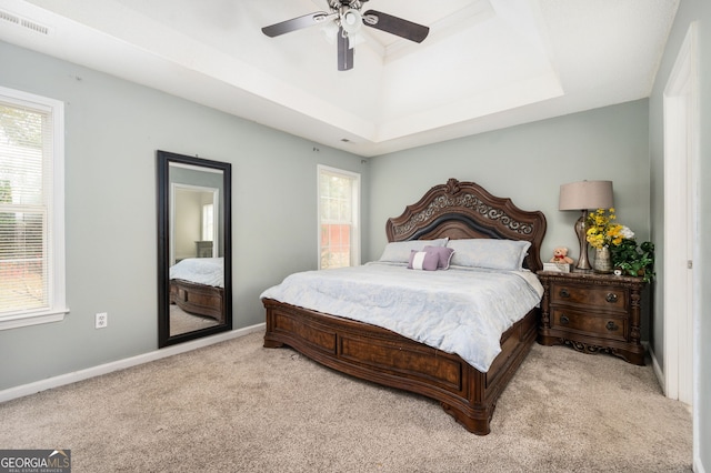 bedroom featuring light carpet, a tray ceiling, and ceiling fan