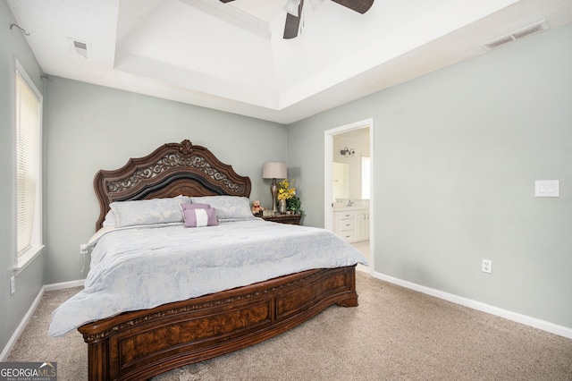 bedroom featuring carpet, ensuite bathroom, ceiling fan, and a tray ceiling