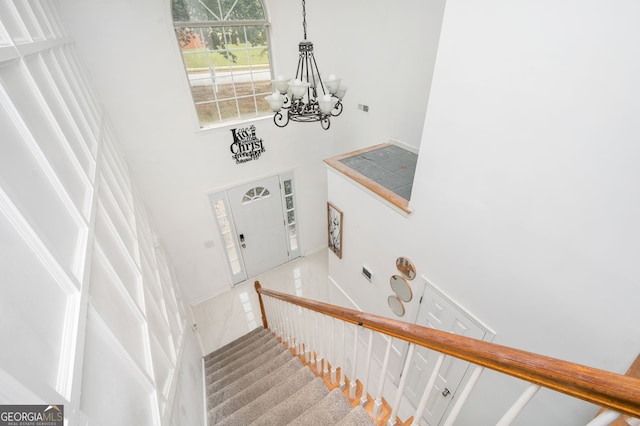 stairs with tile patterned floors, a towering ceiling, and a chandelier