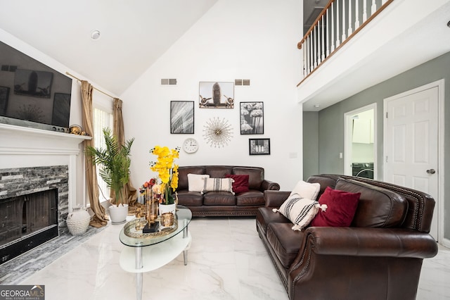 living room with high vaulted ceiling, a stone fireplace, and washer / clothes dryer