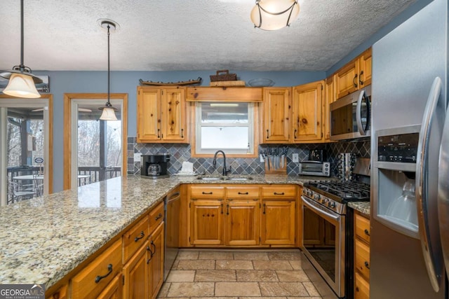 kitchen with pendant lighting, sink, stainless steel appliances, light stone countertops, and a textured ceiling