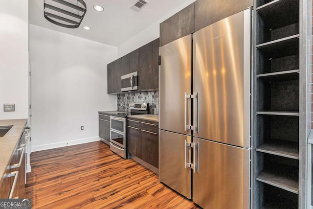 kitchen with dark brown cabinetry, built in features, backsplash, appliances with stainless steel finishes, and light wood-type flooring