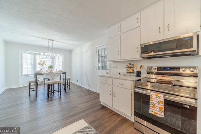 kitchen featuring dark hardwood / wood-style flooring, white cabinetry, stainless steel appliances, and hanging light fixtures