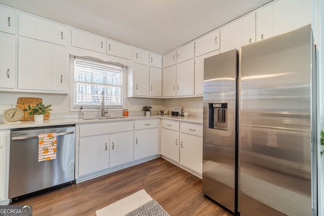 kitchen with a textured ceiling, stainless steel appliances, sink, wood-type flooring, and white cabinets