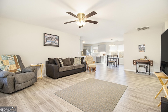 living room with ceiling fan with notable chandelier and light hardwood / wood-style floors