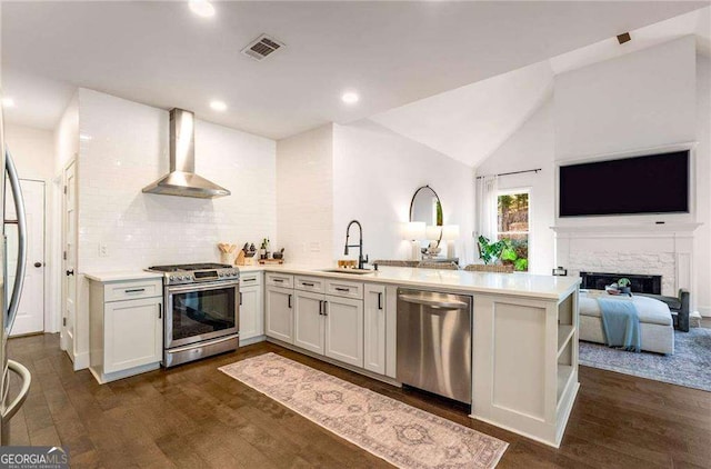 kitchen featuring stainless steel appliances, kitchen peninsula, white cabinets, wall chimney range hood, and lofted ceiling