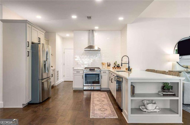 kitchen with stainless steel appliances, wall chimney range hood, dark hardwood / wood-style flooring, white cabinets, and sink