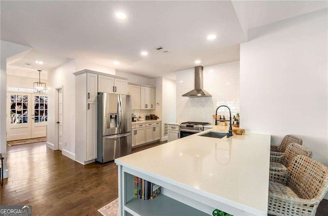 kitchen featuring stainless steel appliances, kitchen peninsula, sink, wall chimney range hood, and tasteful backsplash