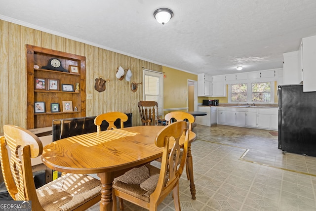 dining area featuring ornamental molding, a textured ceiling, wooden walls, and sink