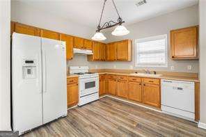 kitchen with dark wood-type flooring, decorative light fixtures, white appliances, and sink