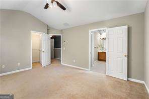 unfurnished bedroom featuring carpet flooring, connected bathroom, vaulted ceiling, and ceiling fan