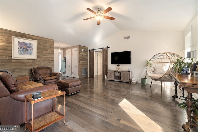 living room with ceiling fan, dark wood-type flooring, a barn door, and wood walls