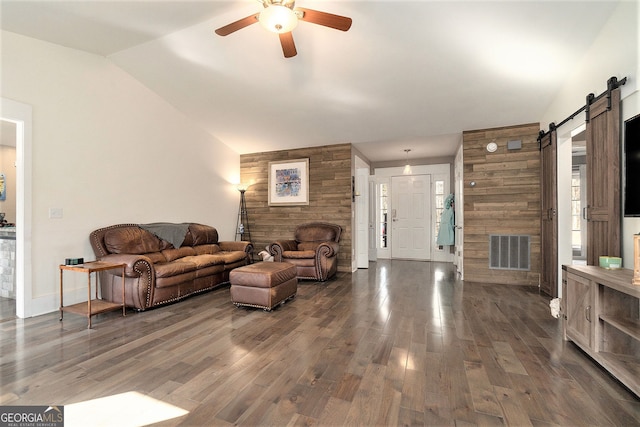 living room with ceiling fan, a barn door, dark hardwood / wood-style floors, and wooden walls