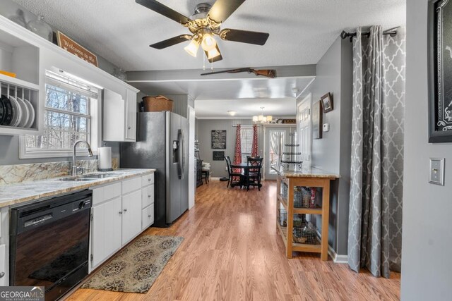 kitchen with light wood-type flooring, ceiling fan with notable chandelier, sink, white cabinets, and black dishwasher