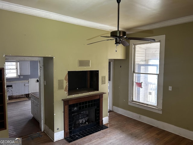 unfurnished living room featuring a tiled fireplace, ceiling fan, crown molding, and wood-type flooring