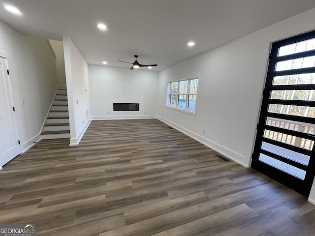 unfurnished living room featuring dark wood-type flooring and ceiling fan