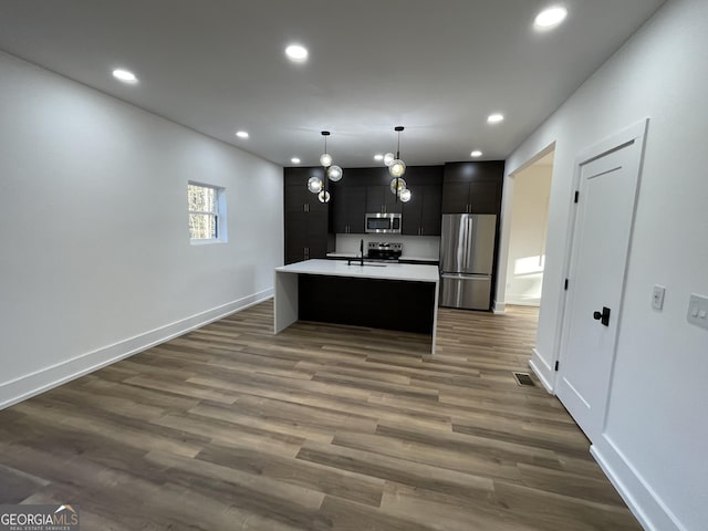 kitchen with decorative light fixtures, sink, a kitchen island with sink, stainless steel appliances, and dark wood-type flooring