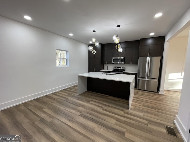 kitchen featuring appliances with stainless steel finishes, decorative light fixtures, hardwood / wood-style floors, and a center island with sink