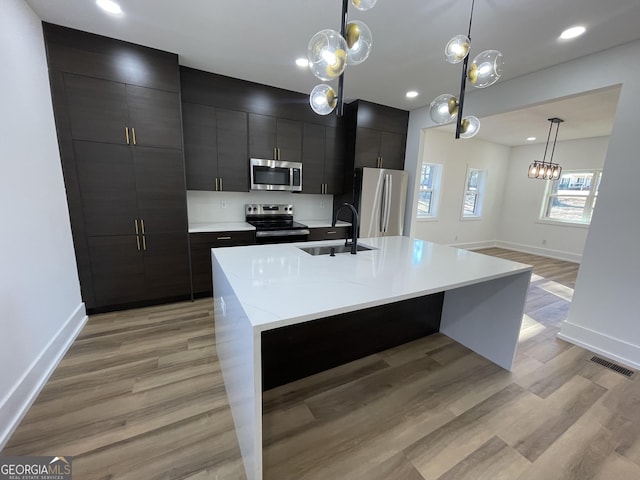 kitchen featuring stainless steel appliances, sink, a kitchen island with sink, and hanging light fixtures