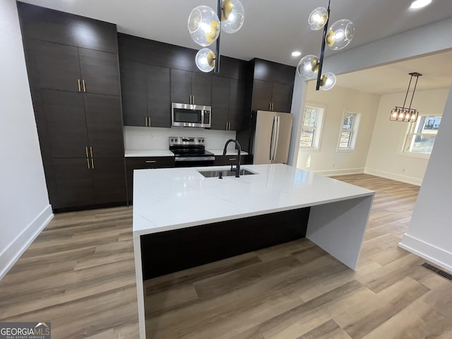 kitchen with appliances with stainless steel finishes, decorative light fixtures, sink, a kitchen island with sink, and light hardwood / wood-style floors