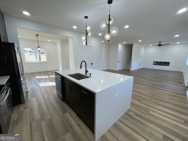 kitchen featuring sink, stainless steel refrigerator, hardwood / wood-style floors, hanging light fixtures, and a center island with sink