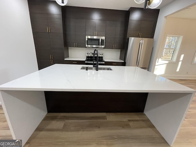 kitchen with sink, stainless steel appliances, light hardwood / wood-style floors, and a center island with sink