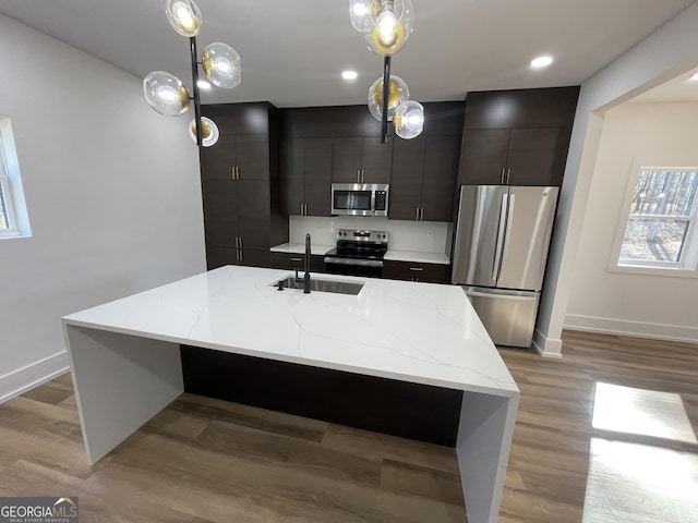 kitchen with pendant lighting, sink, appliances with stainless steel finishes, an island with sink, and light wood-type flooring