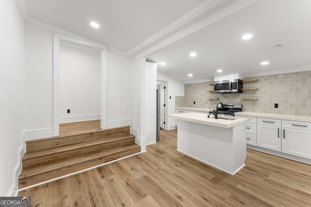 kitchen with light hardwood / wood-style flooring, decorative backsplash, a center island with sink, white cabinets, and appliances with stainless steel finishes