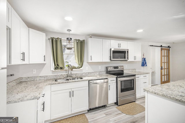 kitchen featuring sink, stainless steel appliances, a barn door, light stone counters, and white cabinets