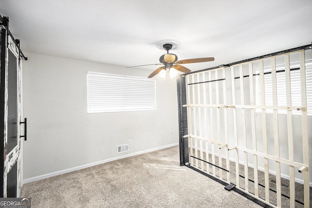 unfurnished bedroom with carpet, a barn door, and ceiling fan