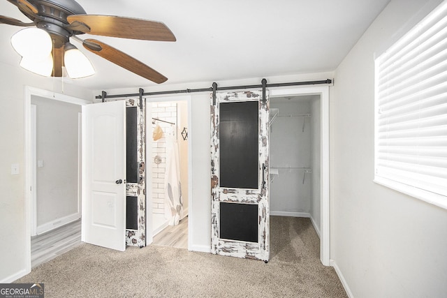 unfurnished bedroom with a walk in closet, ceiling fan, a barn door, light colored carpet, and a closet