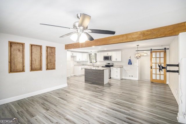 kitchen with a center island, a barn door, appliances with stainless steel finishes, decorative light fixtures, and white cabinetry