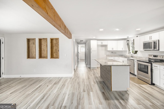 kitchen with light stone countertops, stainless steel appliances, a kitchen island, white cabinets, and light wood-type flooring