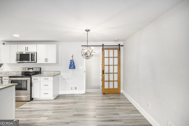 kitchen featuring white cabinetry, a barn door, light stone counters, pendant lighting, and appliances with stainless steel finishes