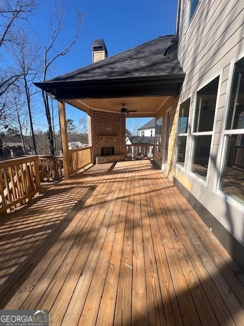 wooden terrace with an outdoor brick fireplace and ceiling fan