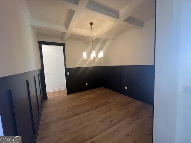 unfurnished dining area featuring beam ceiling, dark wood-type flooring, coffered ceiling, and a notable chandelier