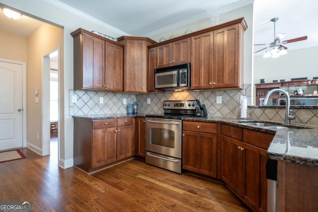 kitchen with appliances with stainless steel finishes, sink, dark stone countertops, dark hardwood / wood-style flooring, and crown molding