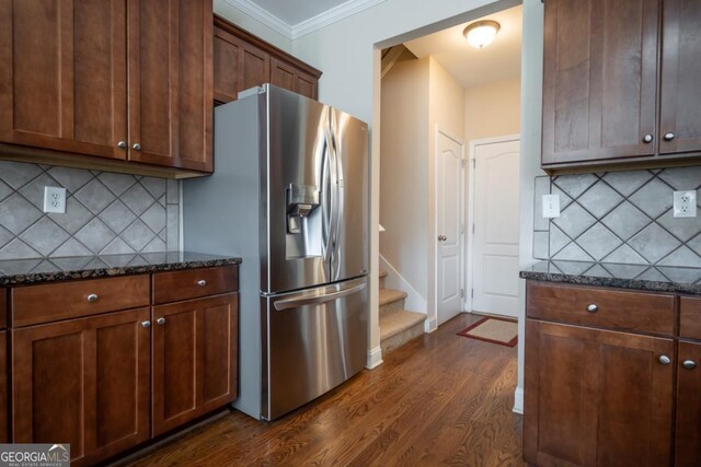 kitchen featuring dark hardwood / wood-style floors, ornamental molding, dark stone counters, and stainless steel fridge