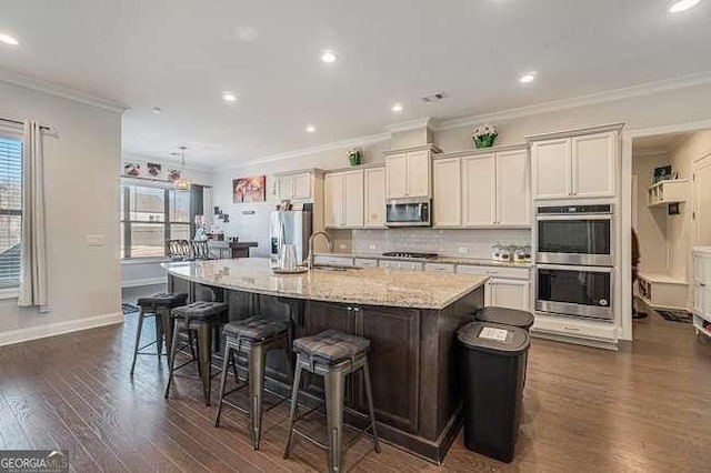 kitchen with light stone countertops, stainless steel appliances, crown molding, sink, and a center island with sink