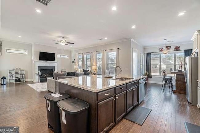 kitchen featuring a center island with sink, sink, ornamental molding, appliances with stainless steel finishes, and dark brown cabinets